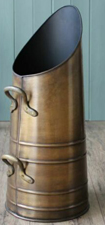 Colour photo of galvanised coal hod, a brassy colour, with two handles and the mouth in an oval shape, higher one one side than the other, so you could swing the hod by the two handles and slide the fuel into the stove. 